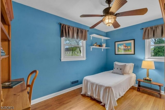 bedroom with baseboards, a ceiling fan, wood finished floors, and visible vents