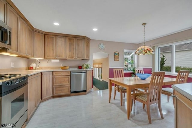 kitchen featuring appliances with stainless steel finishes, a sink, hanging light fixtures, and light countertops