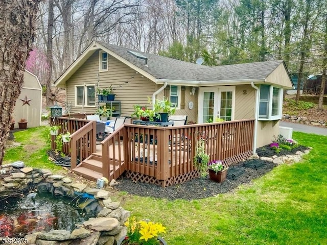 rear view of house with a wooden deck, a small pond, roof with shingles, and a lawn
