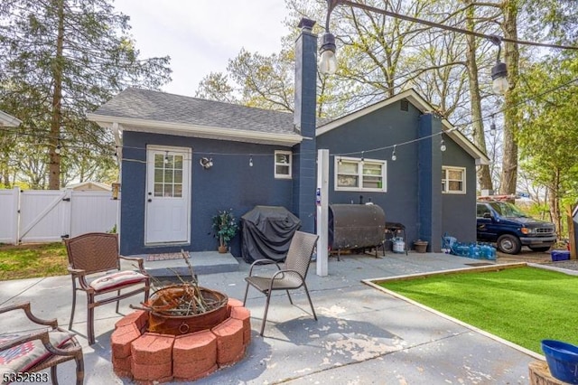 back of property featuring a chimney, a gate, a patio area, a fire pit, and stucco siding