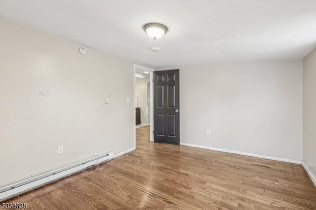 spare room with baseboards, wood finished floors, and a baseboard radiator