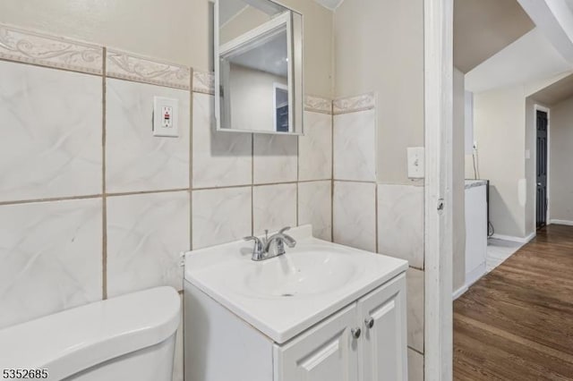 bathroom with toilet, tile walls, wood finished floors, and vanity