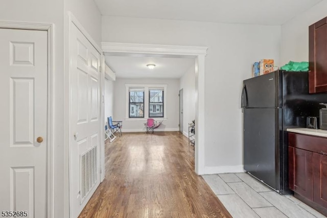 kitchen featuring visible vents, dark brown cabinets, baseboards, freestanding refrigerator, and light wood-style flooring