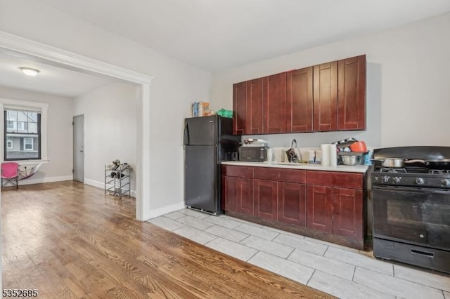 kitchen with dark brown cabinets, light wood-style floors, light countertops, a sink, and black appliances