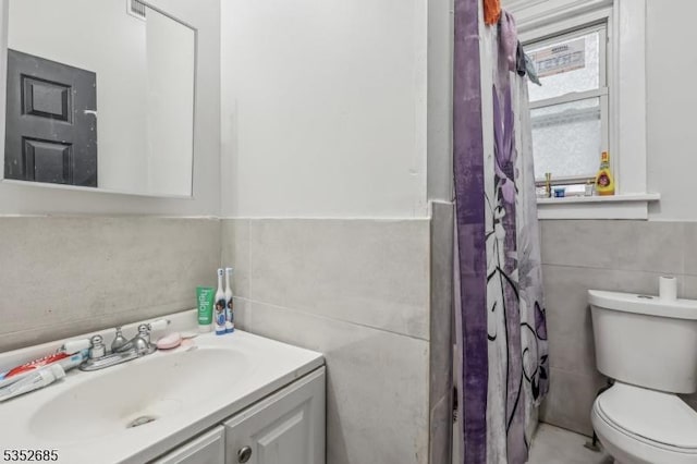 bathroom featuring vanity, toilet, tile walls, a wainscoted wall, and a shower with curtain