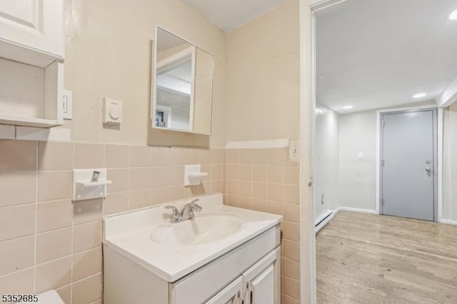 bathroom with tile walls, baseboard heating, wainscoting, wood finished floors, and vanity