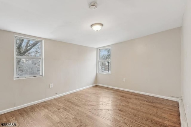 spare room featuring baseboards, wood finished floors, and a wealth of natural light
