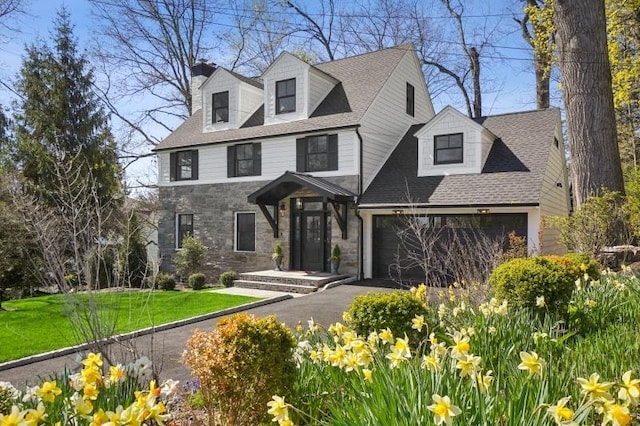 view of front of house with a front lawn, stone siding, a garage, a shingled roof, and aphalt driveway
