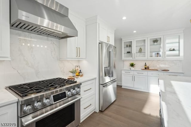 kitchen featuring wall chimney exhaust hood, recessed lighting, white cabinetry, backsplash, and appliances with stainless steel finishes