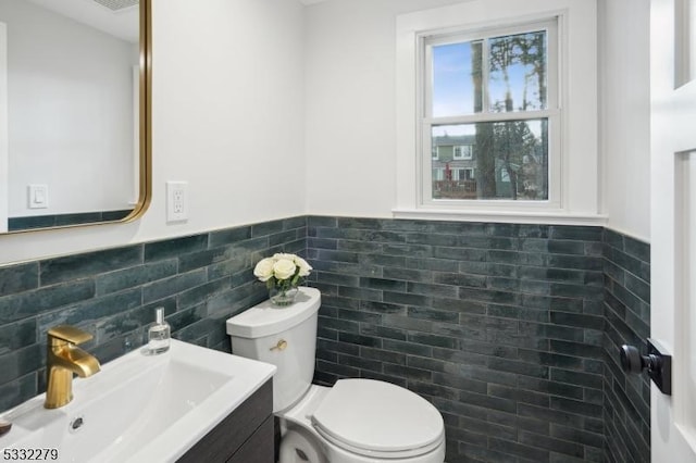 half bathroom featuring tile walls, wainscoting, vanity, and toilet