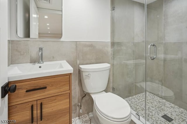 bathroom with tile walls, vanity, a shower stall, and toilet