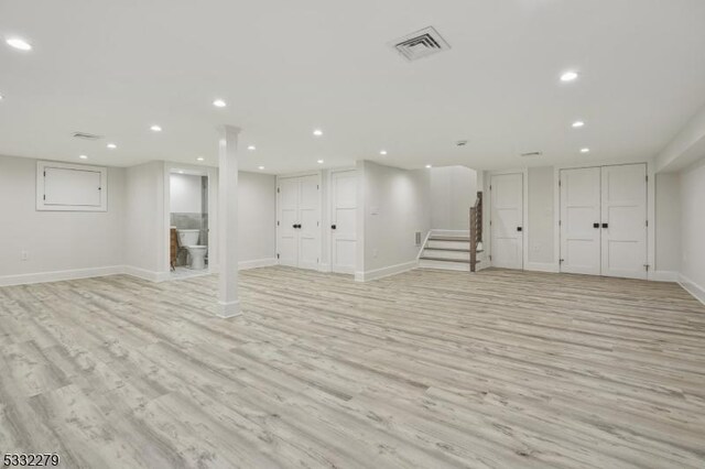finished basement with light wood finished floors, visible vents, recessed lighting, and stairway