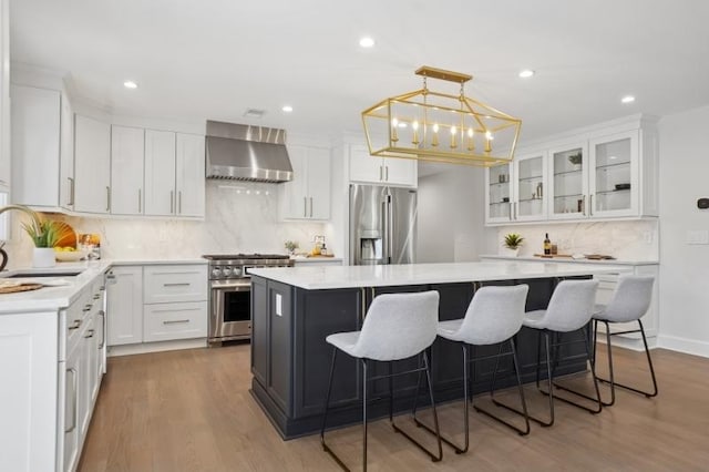 kitchen with wall chimney range hood, a sink, decorative backsplash, appliances with stainless steel finishes, and a kitchen island