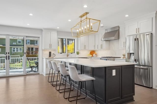 kitchen with wall chimney range hood, a center island, high end fridge, light countertops, and white cabinets