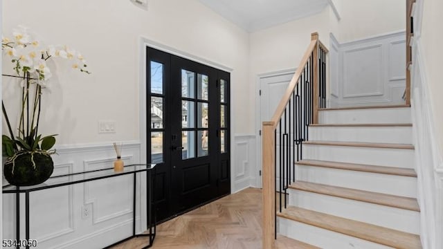 foyer featuring a wainscoted wall, french doors, stairway, and a decorative wall