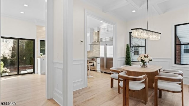 dining space featuring light wood finished floors, a chandelier, beamed ceiling, and a decorative wall