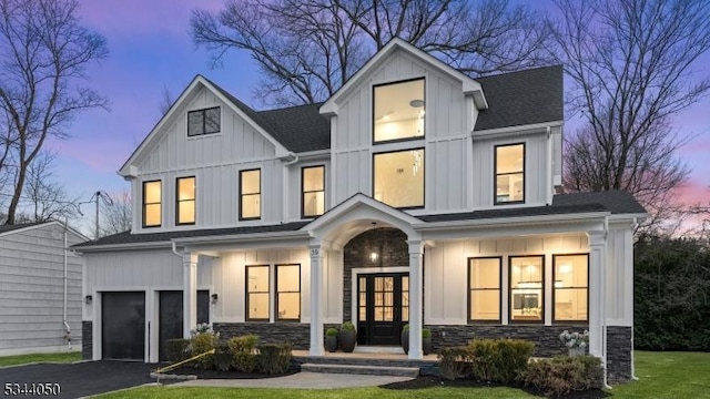 modern inspired farmhouse featuring an attached garage, board and batten siding, driveway, stone siding, and a front yard