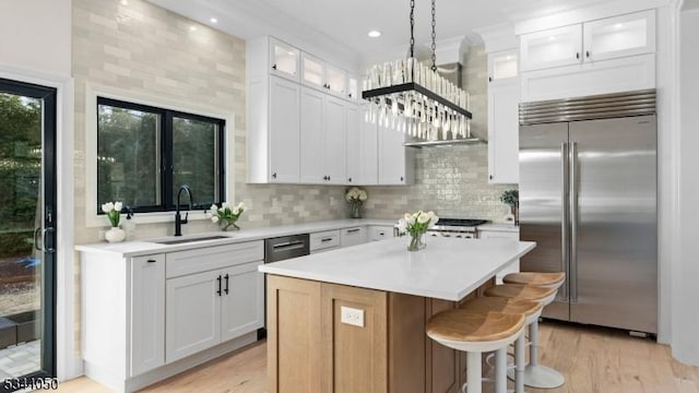 kitchen with light countertops, built in refrigerator, a center island, and a sink