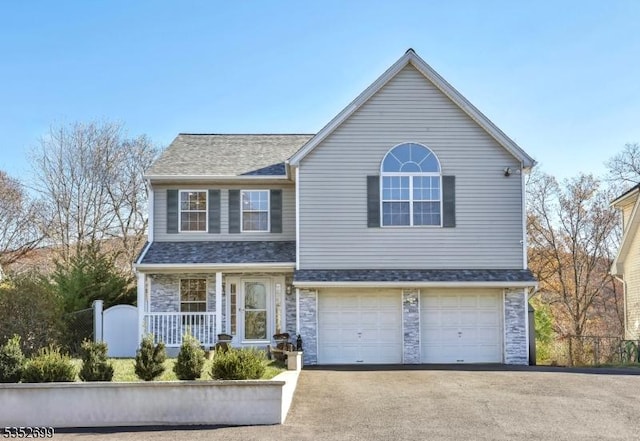 traditional home featuring a garage, stone siding, covered porch, and aphalt driveway