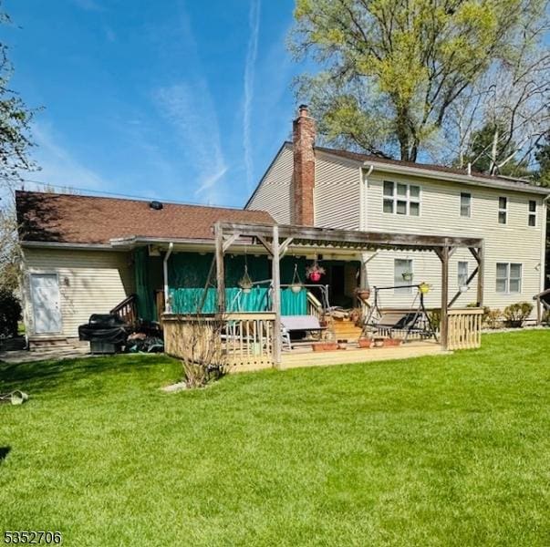rear view of house with a chimney, a pergola, a wooden deck, a patio, and a lawn