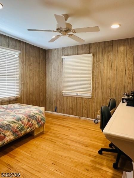 bedroom with ceiling fan, wood finished floors, and wooden walls