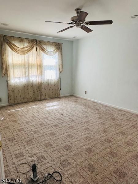 carpeted spare room featuring baseboards and ceiling fan