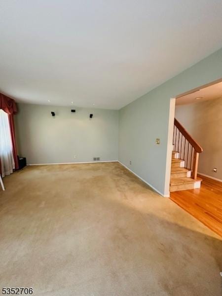 unfurnished living room featuring baseboards, visible vents, light carpet, and stairway