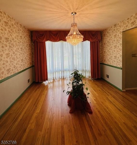 dining space with wallpapered walls, wood finished floors, a wainscoted wall, and a notable chandelier