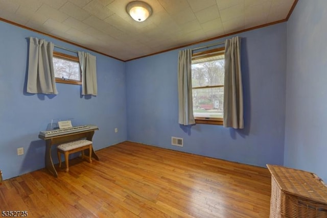 empty room with crown molding, light wood finished floors, and visible vents