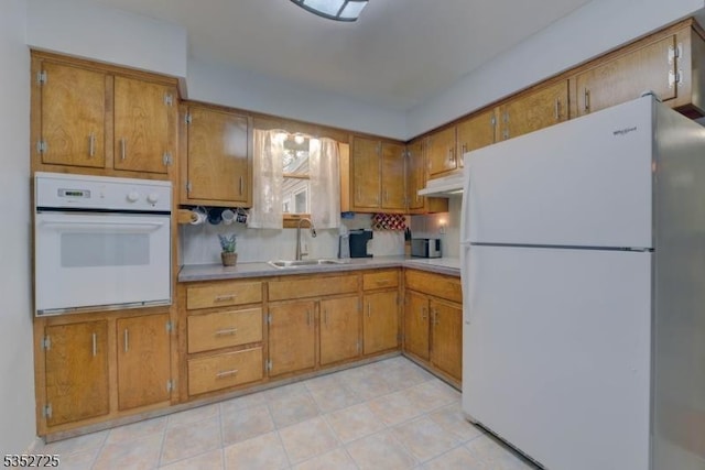 kitchen with a sink, white appliances, brown cabinets, light countertops, and under cabinet range hood