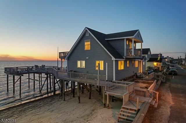 back of house at dusk with a water view and a balcony