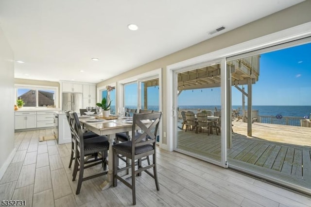 dining area featuring recessed lighting, a water view, light wood finished floors, and visible vents