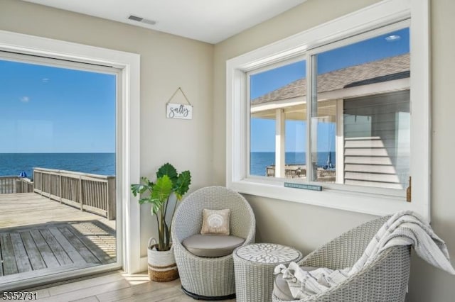 sitting room featuring a water view, visible vents, and wood finished floors