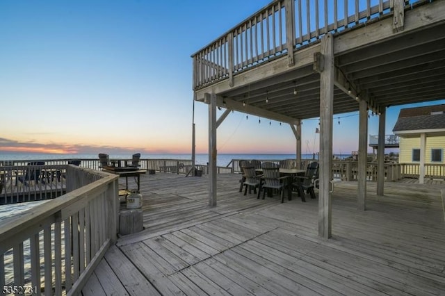 deck at dusk featuring a water view and outdoor dining space