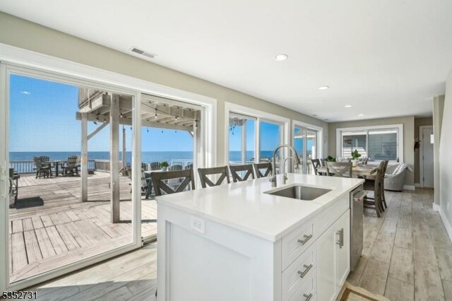 kitchen featuring a sink, light wood-style floors, a water view, visible vents, and a center island with sink
