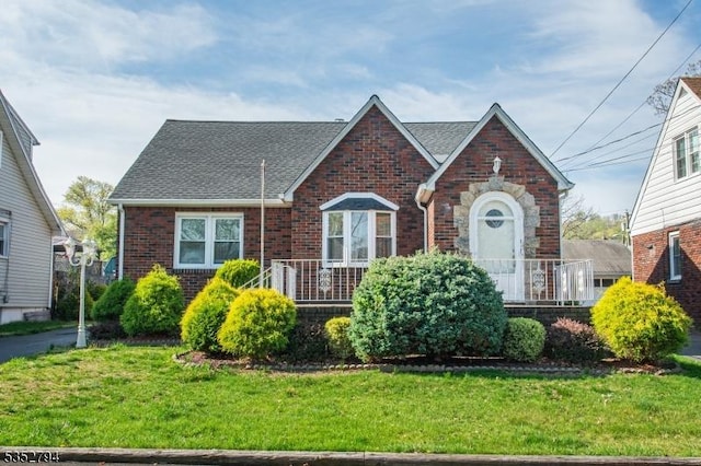 view of front of home featuring brick siding, a front yard, and roof with shingles