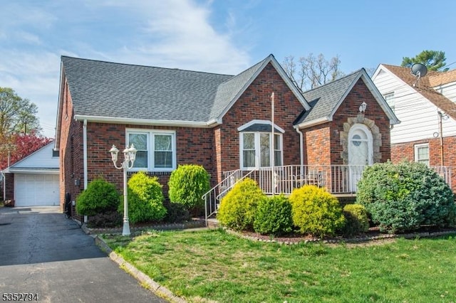 view of front of property with a front lawn, a shingled roof, an outbuilding, a garage, and brick siding