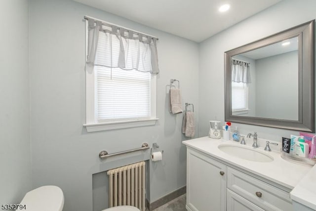 half bath with toilet, baseboards, vanity, and radiator