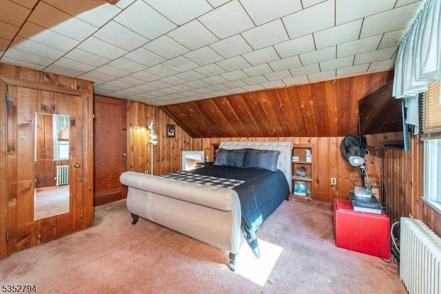 carpeted bedroom with lofted ceiling, wood walls, and radiator