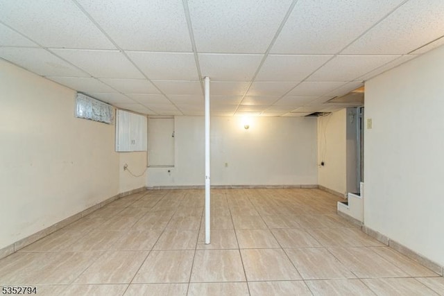 finished below grade area featuring a paneled ceiling, baseboards, and light tile patterned floors