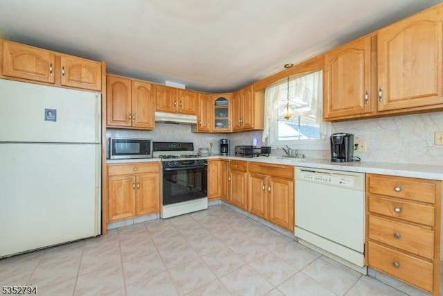 kitchen featuring under cabinet range hood, light countertops, a sink, white appliances, and tasteful backsplash