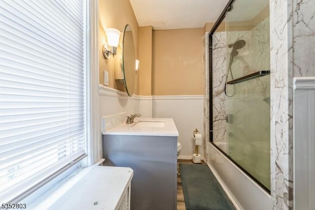 full bath featuring shower / bath combination with glass door, wood finished floors, toilet, and vanity