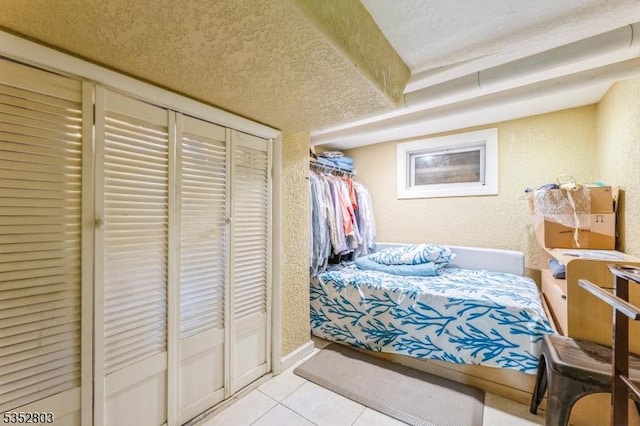 bedroom featuring light tile patterned floors, a textured wall, and a textured ceiling
