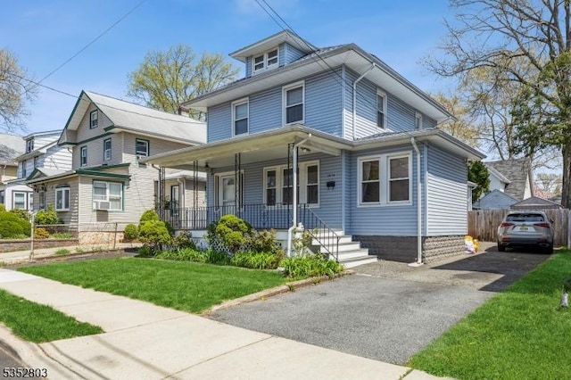 traditional style home with covered porch, fence, and a front yard