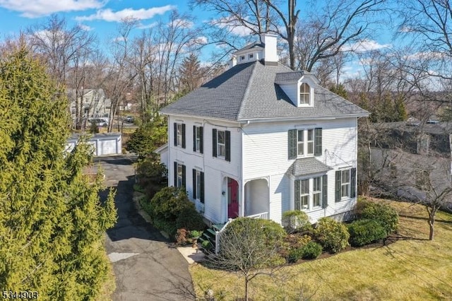 view of front of house with a shingled roof, an outdoor structure, and a chimney