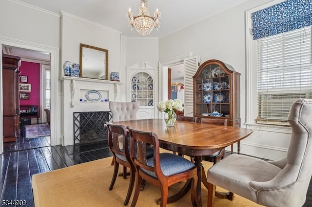 dining room with a fireplace with flush hearth, dark wood-style floors, an inviting chandelier, and ornamental molding