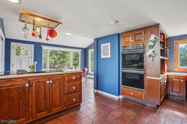 kitchen featuring wallpapered walls, light countertops, vaulted ceiling, dobule oven black, and baseboards