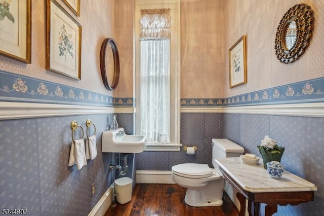 half bathroom with wallpapered walls, hardwood / wood-style flooring, toilet, and a healthy amount of sunlight