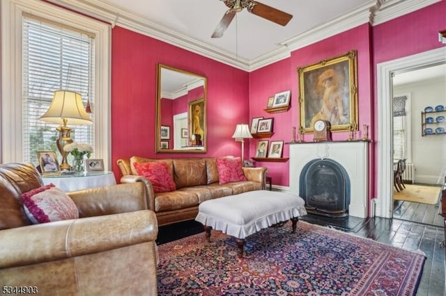 living area featuring wood-type flooring, crown molding, baseboards, a fireplace, and ceiling fan