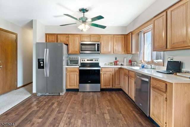 kitchen featuring stainless steel appliances, a sink, dark wood-style flooring, ceiling fan, and light countertops
